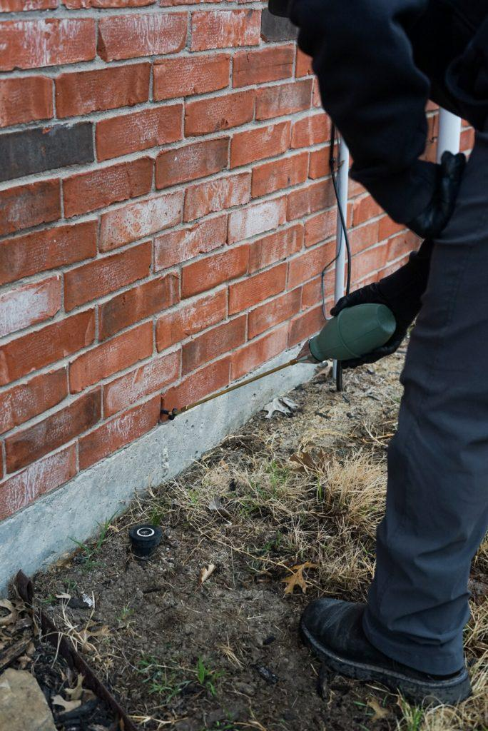 A technician dusting the inside of a brick wall for scorpions.